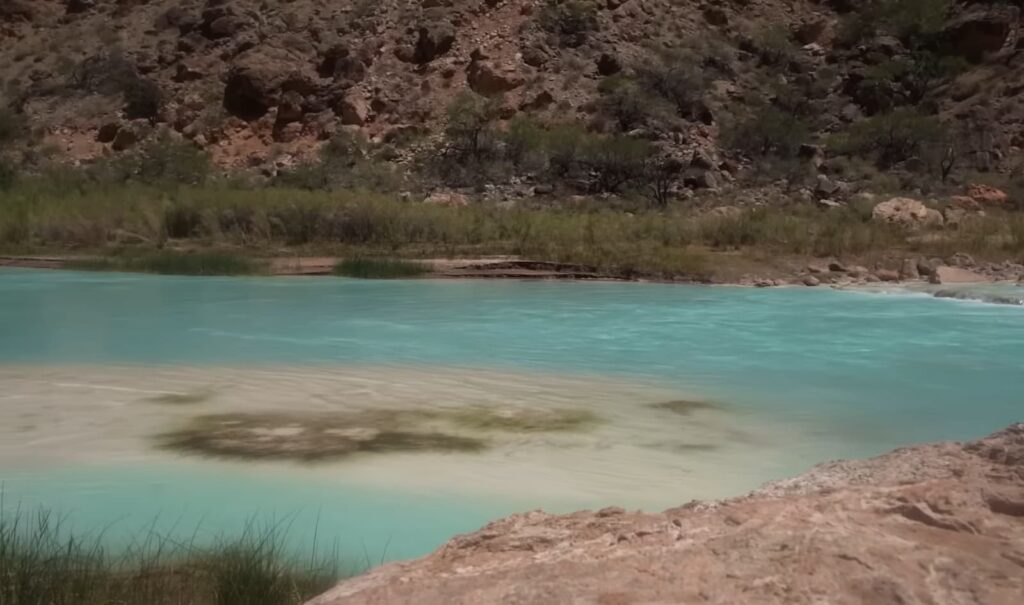 Close-up of a serene, milky turquoise river bordered by rocks and shrubs